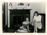 Betty Cue is seated showing a Curtiss P-40 Warhawk model plane to a cadette in the Memorial Union, 1943