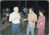 Earl O. Heady outside at an evening social event in Thailand talking with a man and a woman, 1983.