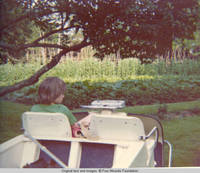 John, Jr. sitting in golf cart by vegatable garden