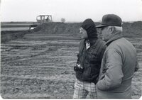 Two men stand near earthmover in a field