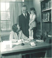 Man holds a young girl standing on a desk in an office, The University of Iowa, 1940s