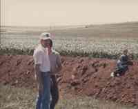 Two men watch boy sitting on bulldozed dirt