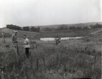 Two unidentified men stand in field by pond
