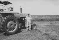 Man in White Hat, Shirt and Overalls Standing by White Tractor