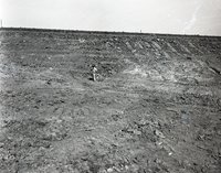 Unidentified Man Looks Down at Pipe in Rocky Soil