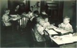 Children sitting at small dinner tables with a woman, The University of Iowa, 1920s