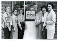 Six women stand on either side of a welcome sign for the Agricultural Stabilization Conservation Service,<br />
 Davis County Office
