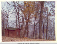 Corgy by cabin outhouse in Fall 