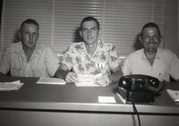 Three unidentified men sit in office at a desk
