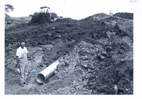Clyde Small poses beside outlet end of pipe spillway, 1966
