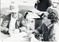 1978 Two men sit at a table in a field