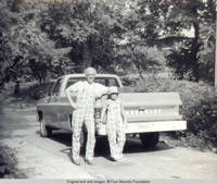 Bill and John, Jr. leaning on truck wearing matching plaid overhalls