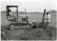 1979  Man on Bulldozer in front of Man putting pipe in the ground